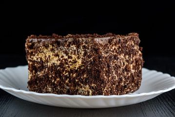 a piece of chocolate cake on a white plate on a dark wooden background. Homemade baking.Close-up view.