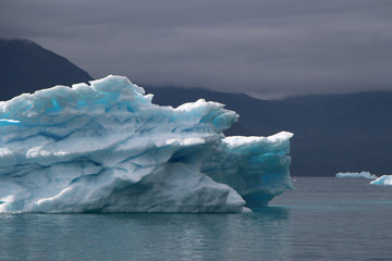 blue iceberg with lightblue spots inside of it and also with dramatic mood of the sky in the atlantic ocean