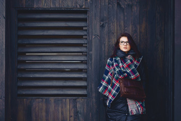beautiful girl in eyeglasses and a scarf against a wooden wall