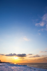 a beach under snow and a cold, ice-covered sea during sunset