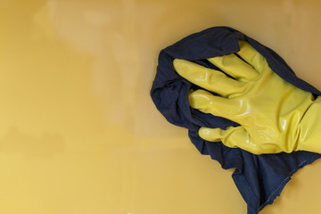 A yellow glove hand wipes the yellow wall. The concept of cleanliness