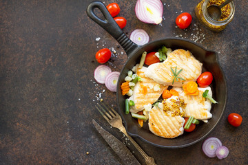 Grilled chicken fillet and various vegetables on a cast-iron frying pan. Copy space, top view flat lay background.