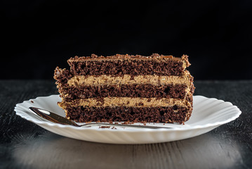 a piece of chocolate cake on a white plate on a dark wooden background. Homemade baking.Close-up view.
