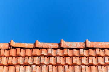 An old roof with burnt tiles. Roof in village house against a blue sky background.