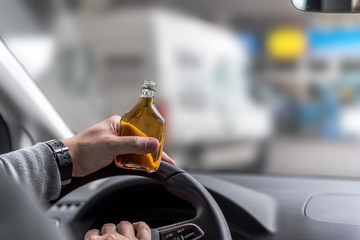 An elderly man drives a car and holds a bottle of alcohol in his hand and drinks it while driving. Concept: transportation and safety or health
