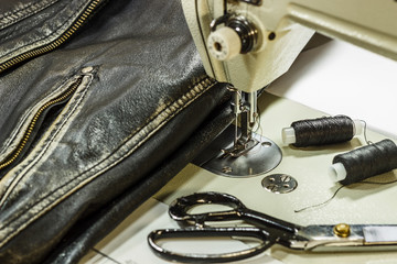 Sewing leather jacket repairing leather jacket scissors, thread, sewing machine, close-up.