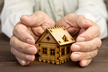Old man protecting house model with hands.Risk insurance.The concept of mortgages and Bank loans. Poverty. Rental property.