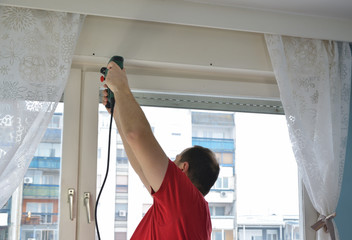 Man drilling a hole in a window frame in order to install an indoor blind