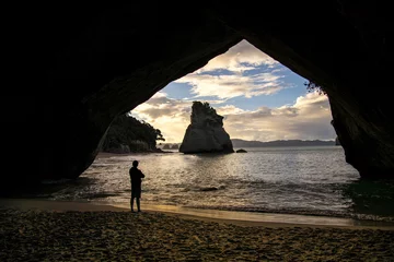 Fotobehang A man gazes out at Cathedral Cove from inside a cave on the Coromandel Peninsula near Auckland, New Zealand © Chris