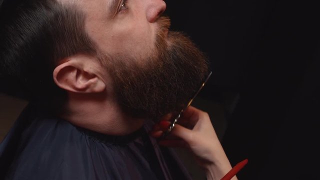 woman barber cuts beard client with scissors, close-up