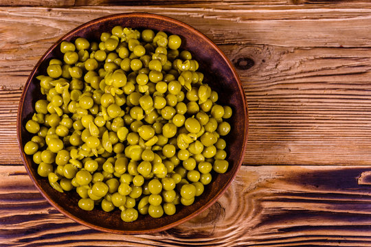 Ceramic plate with canned green pea on wooden table. Top view