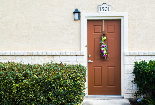 brown townhouse door in a tan limestone and stucco building with spray of flowers and green hedges