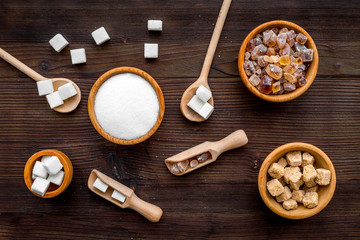 Sugar background on dark wooden table. Bowls with different kinds of sugar. Top view