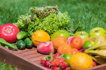 Various vegetables and fruits on a wooden tray against a background of green grass