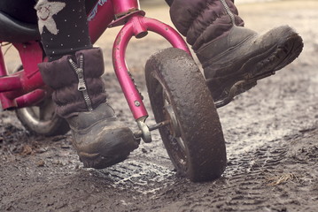 Naklejka premium Child riding tricycle. The child rides a tricycle on a wet road