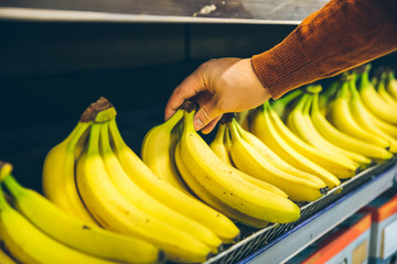 mans hand take bananas from shelf of store