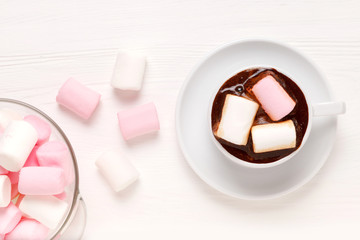 White Cup with coffee and white and pink marshmallow on light wood surface