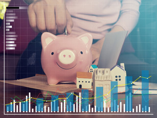 Close up hand putting coin into piggy bank for saving money.young smart woman holding money coin and prepare to put the coin in piggy bank.Mortgage concept by money house from the coins