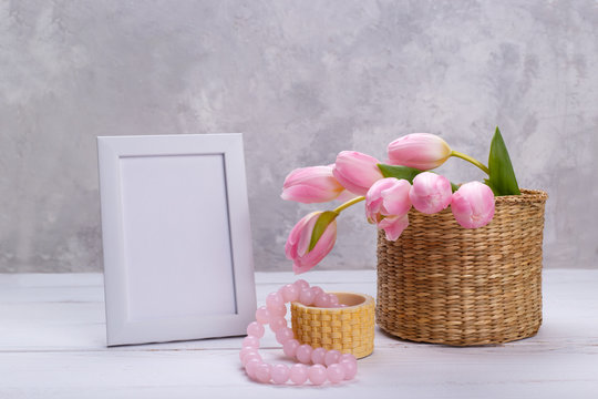 Bouquet of pink tulips in a wicker basket and empty picure frame on light gray background