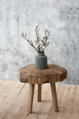 Wooden stool with braches of plant in grey bottle on grey texturized background - obrazy, fototapety, plakaty