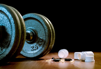 Steroid pills and capsules with dumbbell weight in the background - doping in sport.