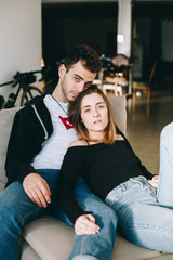 Stylish and chic trendy hip hipster couple of millennial teenagers or models at photoshoot pose on sofa or armchair in cool industrial loft with bikes on background, look in camera, influencers