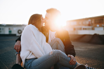 Tender and sensual young man embraces and hugs his lover or girlfriend to protect from cold on sunset lit rooftop, kisses her gently as image of true love and real emotions of young millennials