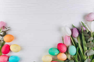 Easter composition with colored eggs and tulips on a white wooden background.