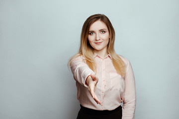 Body language and emotions. serious woman  blonde in a pink blouse on a white background.  girl stretching his arm, smiling pleasantly, greeting business partners before presentation