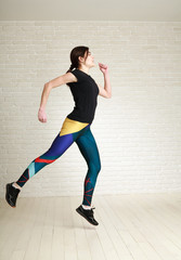 Jumping woman doing fitness exercises in studio on brick wall background