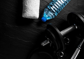 Dumbbell, bottle of water and white towel on black background. Gym accesories.