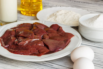 Raw liver on a white plate on a wooden background. A set of products for cooking fried liver egg oil salt flour. Food ingredient. Selective focus.