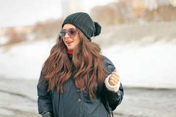 young attractive woman fashionista with red lipstick walking in a black down jacket and glasses in the winter on the street
