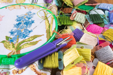 The process of cross-stitch. Canvas on hoops, needles, embroidery floss and pattern.