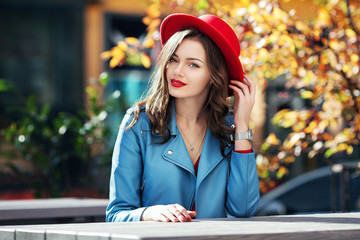 Beautiful happy smiling girl with long hair, red lips, wearing stylish hat, blue jacket posing in...