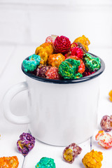 Brightly Colored Candied Popcorn, white background. Image of Junk food, fruit flavored popcorn. Colorful, rainbow, candy coated popcorn in old metal cup. Isolated on white selective focus 