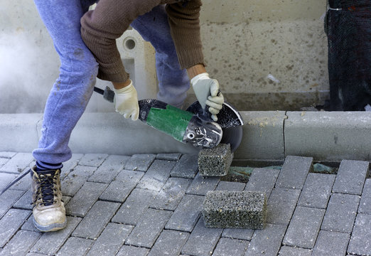Worker cuts a tile to size with an electric grinder to complete the self-locking paving
