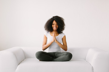 An African American young women sitting in the lotus position on white bed