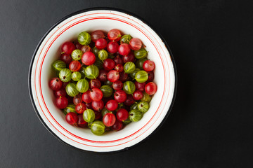 Fresh gooseberries in an enamel bowl on dark background