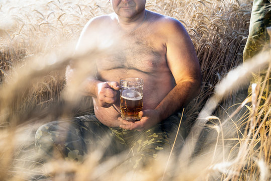 large glass of light beer is held by a fat man