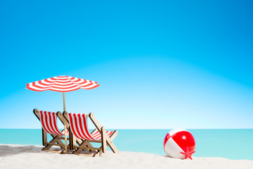 Two lounge chairs with parasol and beach ball on the coast