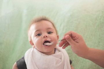 Blue eyed baby boy eating yogurt in the spoon