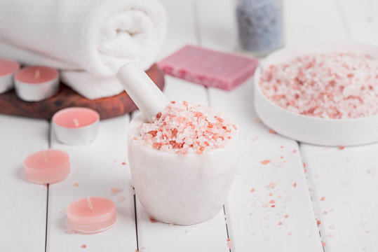 Cleansing spa accessories with himalayan salt, rose soap petals and exfoliating bathroom products on distressed white wood background.