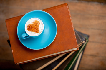 Cup of coffee with heart shape cream on books