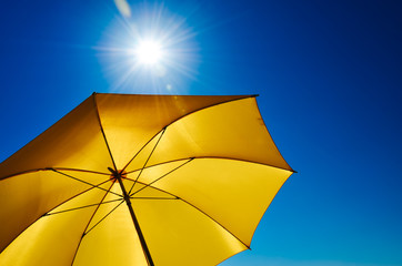 Gelber Sonnenschirm mit strahlend heller Sonne und blauem Himmel - obrazy, fototapety, plakaty
