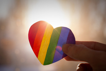 LGBT day concept, hand holds a heart painted like a LGBT flag, silhouetted against sun