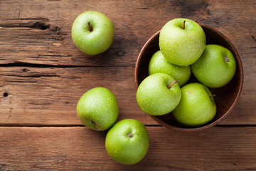 Ripe green apples in a wooden bowl on an old rustic table. Useful fruits on wooden background. Top view with copy space