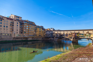 Obraz premium Arno river with unknown man on kayak, houses and old Ponte Vecchio bridge, Florence, Tuscany, Italy