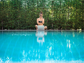 thoughtful woman sitting & reflecting at the pool with her laptop