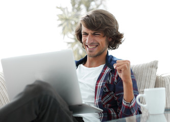 very happy guy with a laptop sitting near a coffee table.